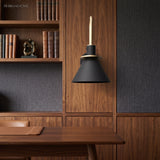 Black cone wall sconce mounted on a walnut bookcase above a desk