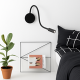 Black reading light on a white wall above a bed and plant