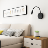 Black reading light above a bedside table beside a framed print