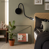 Black reading light lit on a green wall beside a cane headboard