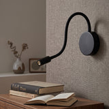 Black gooseneck reading light above a bedside table and open book