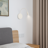 White reading light lit on a pale wall beside a bed