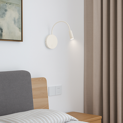 White reading light lit on a pale wall beside a bed