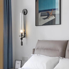 Black fluted glass sconce lit above a bed with white pillows