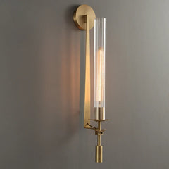 Gold fluted glass sconce lit on a grey wall seen at an angle