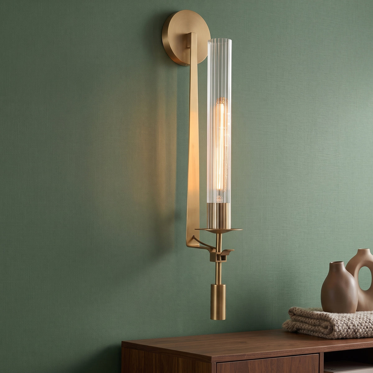 Gold candle style wall sconce with a fluted glass tube on green