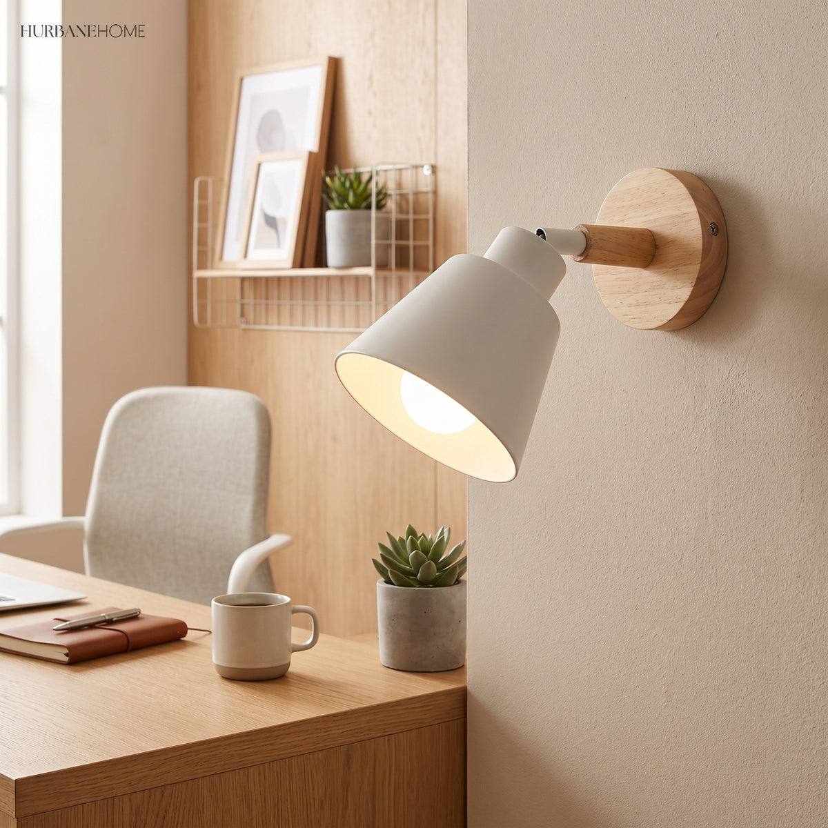 White bell shade sconce lit above a desk with a mug and plant