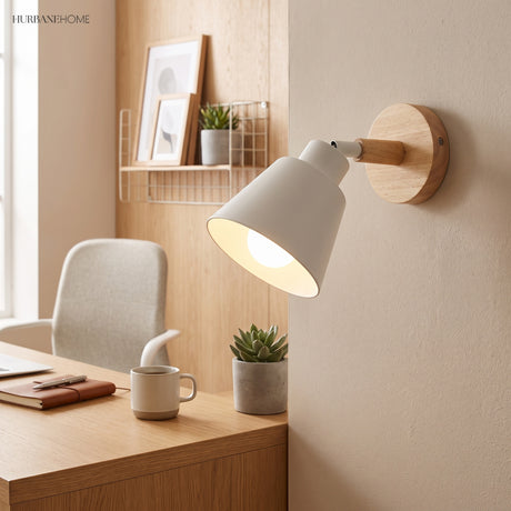 White bell shade sconce lit above a desk with a mug and plant