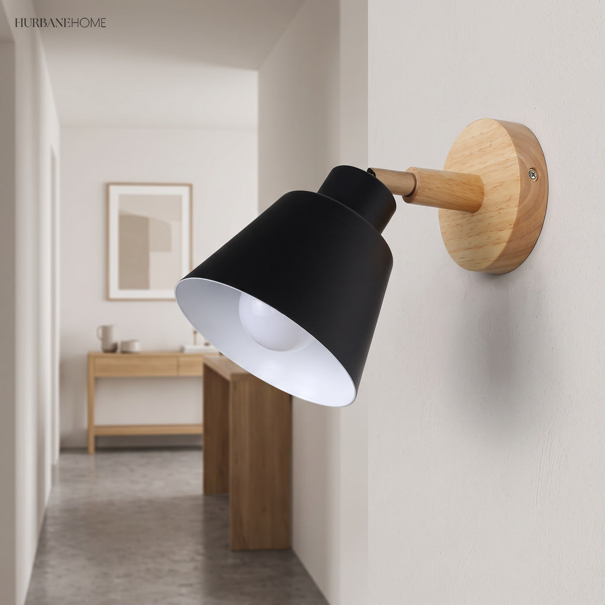 Black bell shade sconce lit in a hallway beside a console table