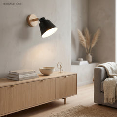 Black bell shade sconce on a wood mount lit above a sideboard