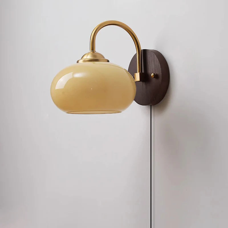 Beige oval glass sconce with brass arm and plug-in cord, studio