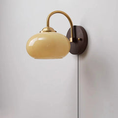 Beige oval glass sconce with brass arm and plug-in cord, studio