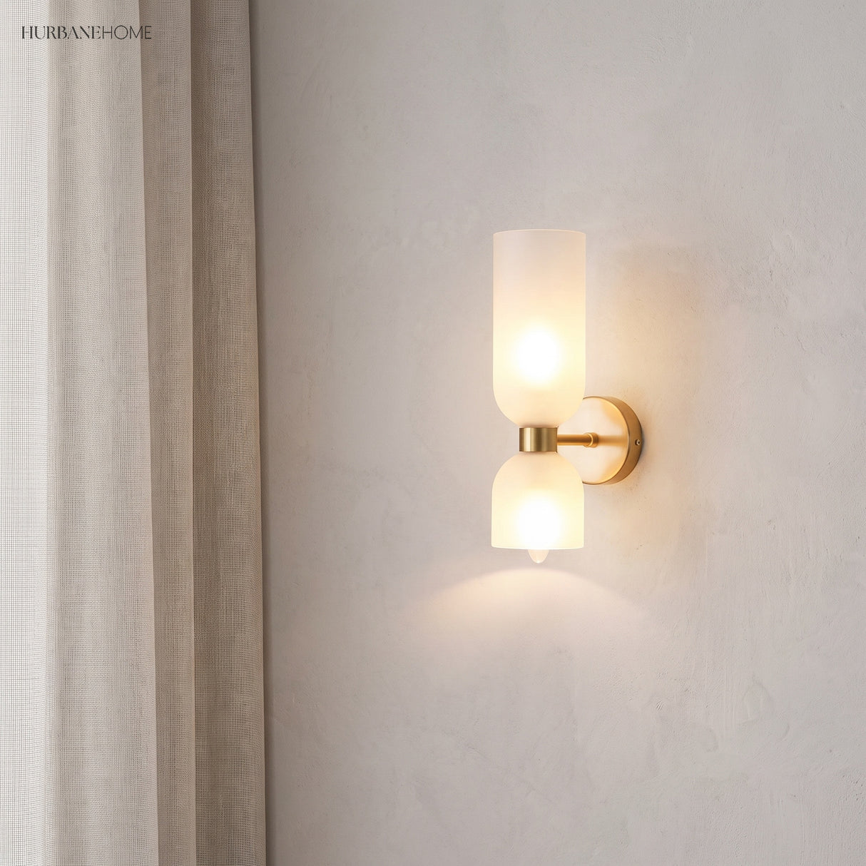 Glass wall sconce lit beside linen curtains in a quiet corner