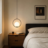 Black round frame glass globe pendant lit above a wood bedside table in a bedroom