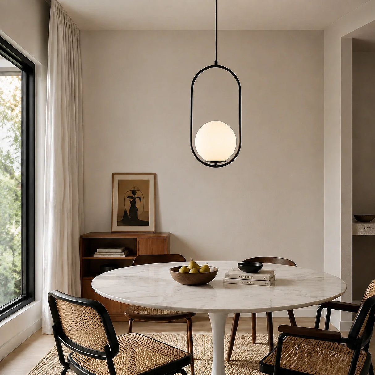 Black oval frame glass globe pendant over a round marble dining table and rattan chairs