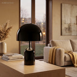 Black gloss table lamp on a timber console beside books and a window at dusk