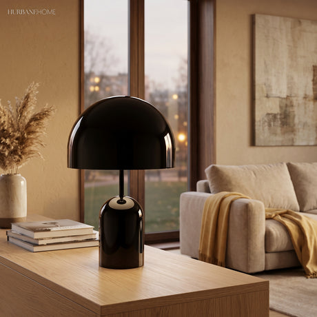 Black gloss table lamp on a timber console beside books and a window at dusk