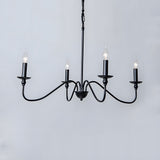 Four light black candle chandelier with curved arms against a pale grey wall