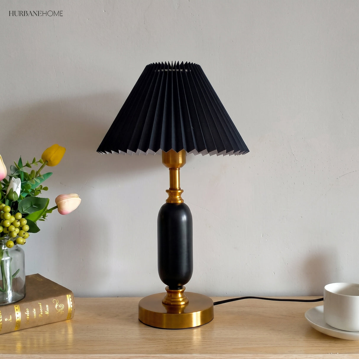 Black pleated shade table lamp beside tulips and a book on a console