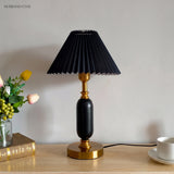 Black pleated shade table lamp beside tulips and a book on a console