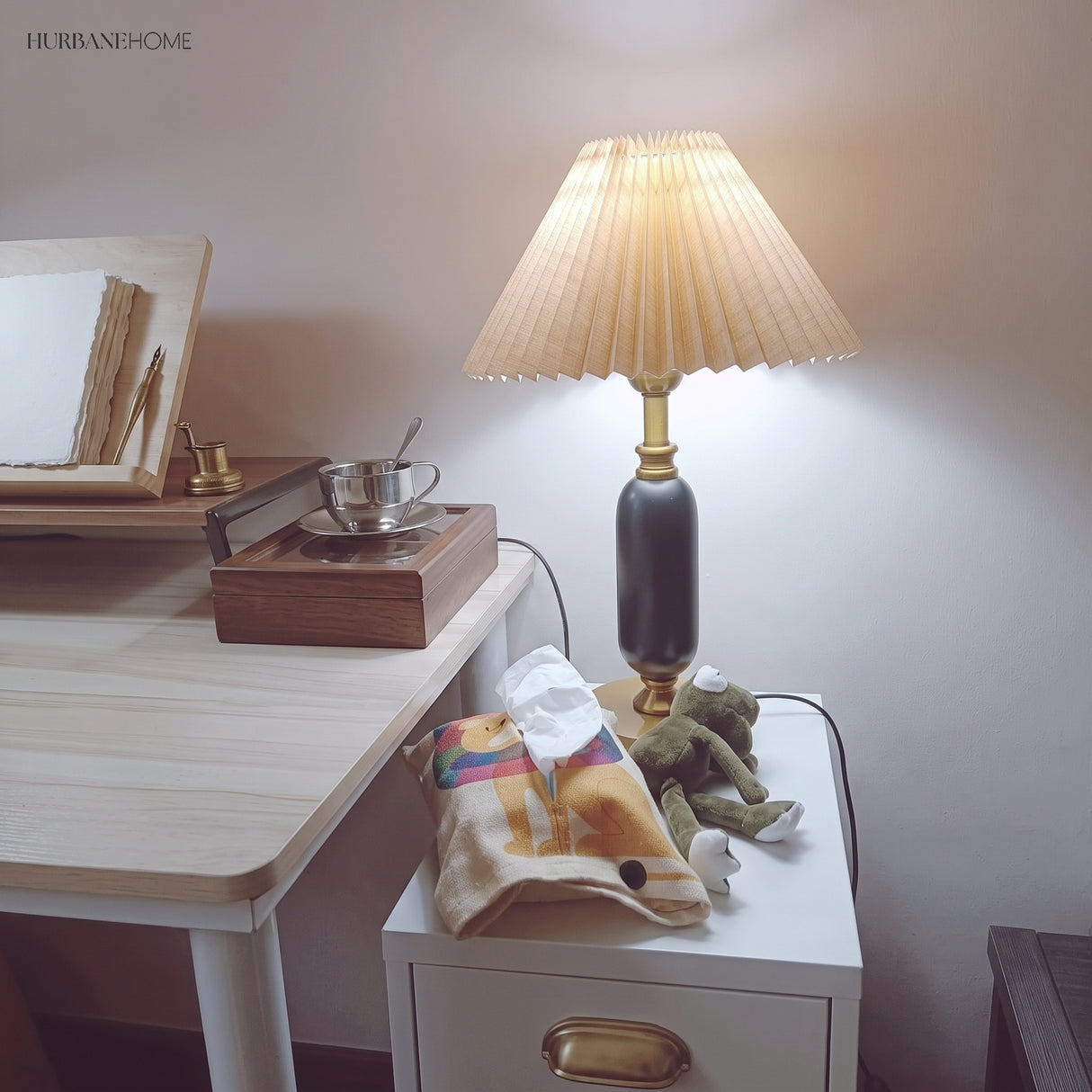 Lit black pleated table lamp glowing on a bedside drawer unit