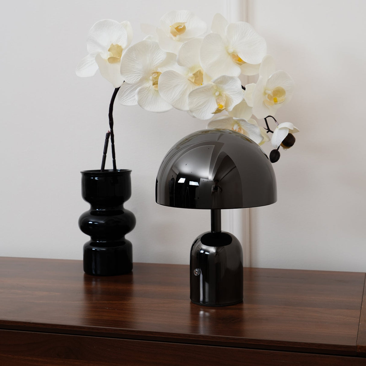 Black dome lamp and an orchid in a ribbed vase on a walnut sideboard