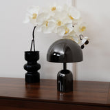 Black dome lamp and an orchid in a ribbed vase on a walnut sideboard