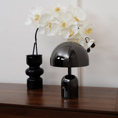 Black dome lamp and an orchid in a ribbed vase on a walnut sideboard