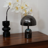 Side profile of the black gloss lamp next to a tall white orchid stem