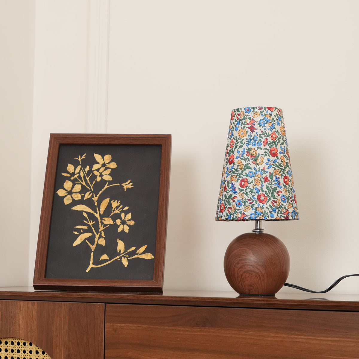 Blue floral shade lamp beside a gold botanical print on a dark cabinet