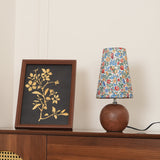 Blue floral shade lamp beside a gold botanical print on a dark cabinet
