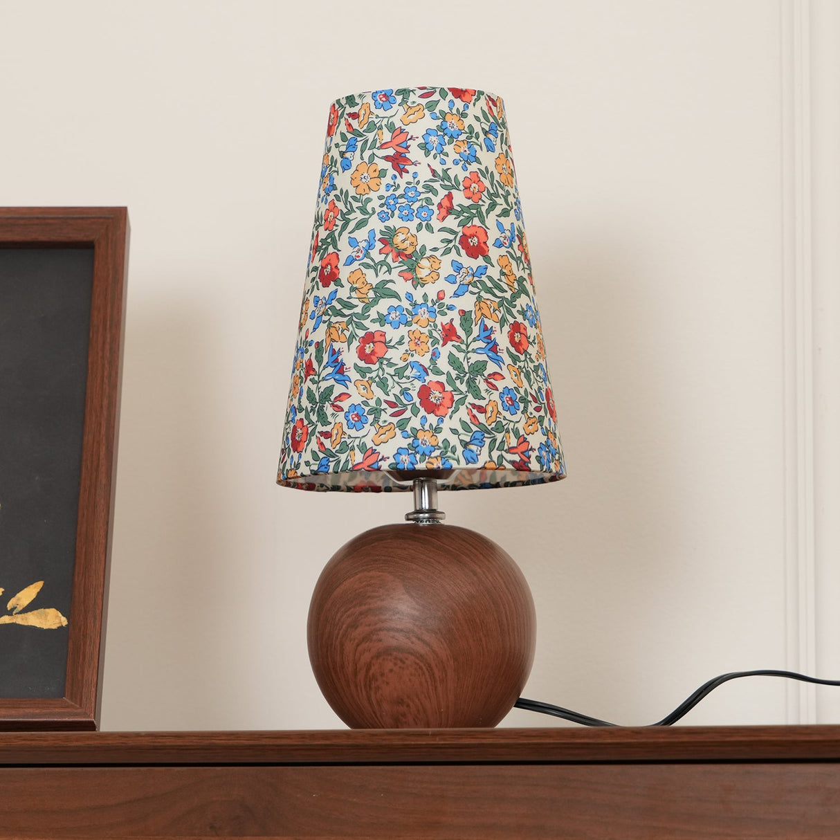 Blue and red floral shade lamp on a walnut sideboard beside framed art