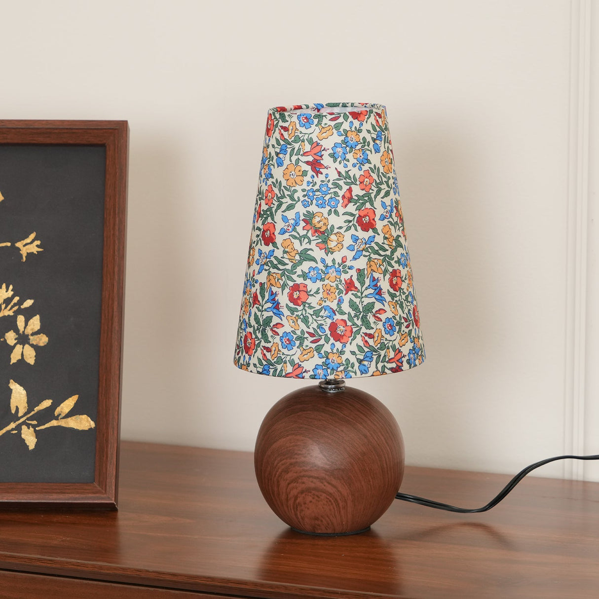 Blue ground floral shade lamp lit on a sideboard with the cord visible
