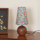 Blue ground floral shade lamp lit on a sideboard with the cord visible