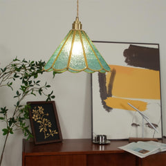 Blue glass pendant lit above a desk with trailing foliage and framed art