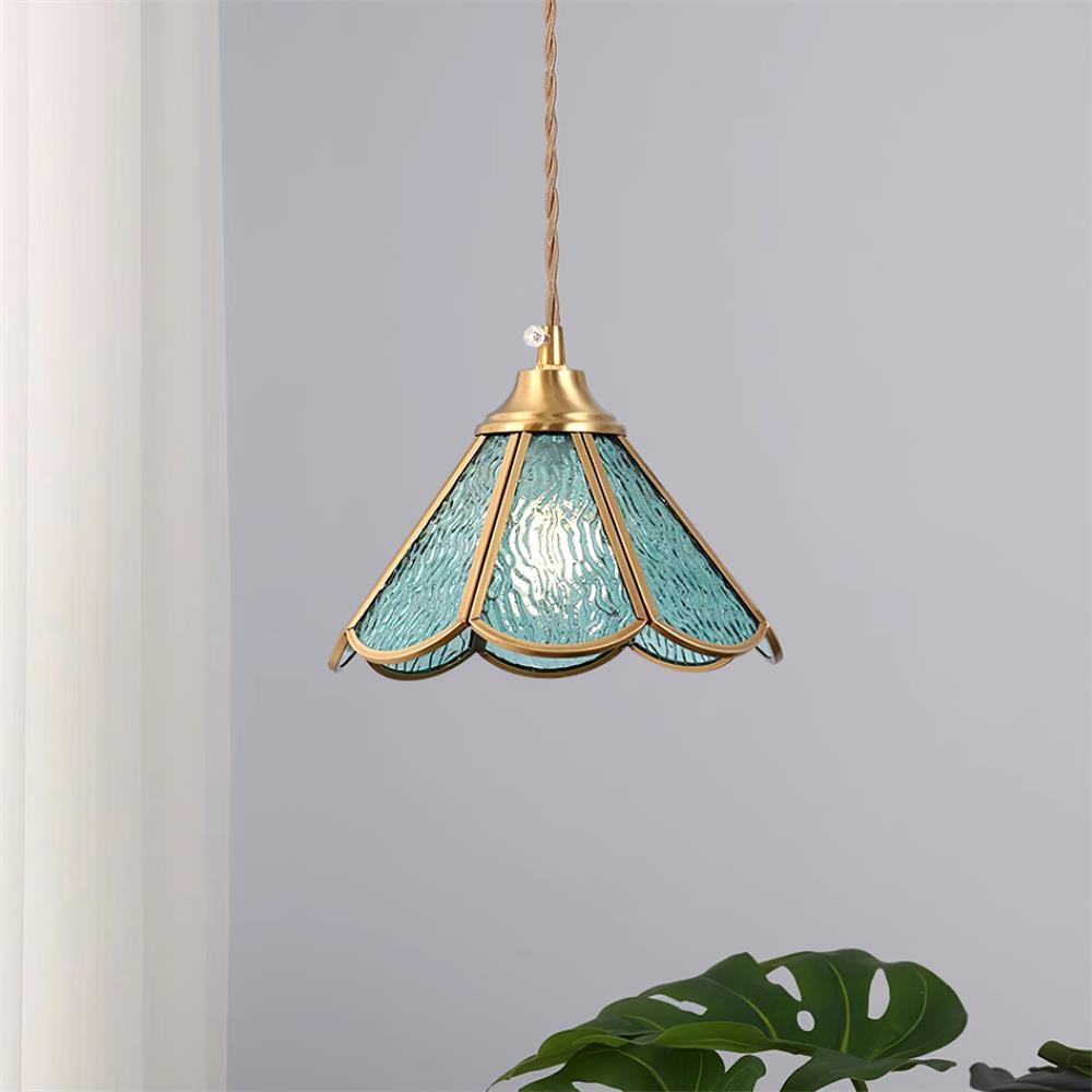 Blue glass pendant hanging against a plain wall beside a large green leaf