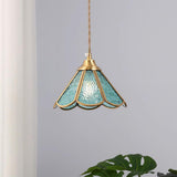 Blue glass pendant hanging against a plain wall beside a large green leaf