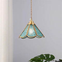 Blue glass pendant hanging against a plain wall beside a large green leaf