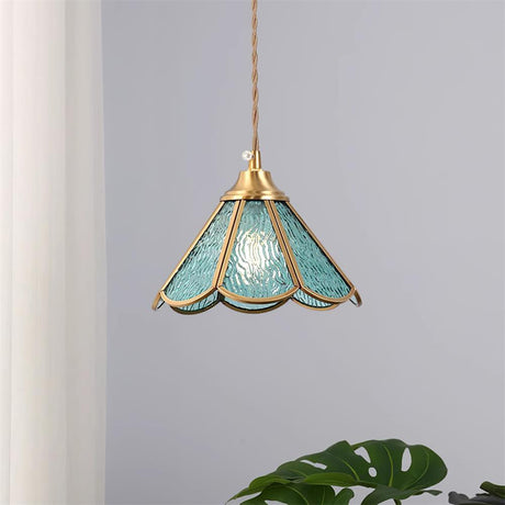Blue glass pendant hanging against a plain wall beside a large green leaf