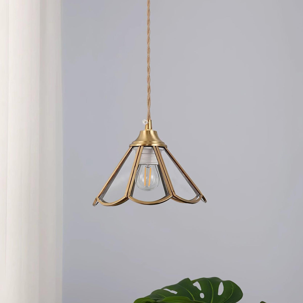 Open brass framed pendant unlit beside a curtain with the bulb showing