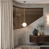 Brass stem globe pendant beside a curved mirror and linen curtain