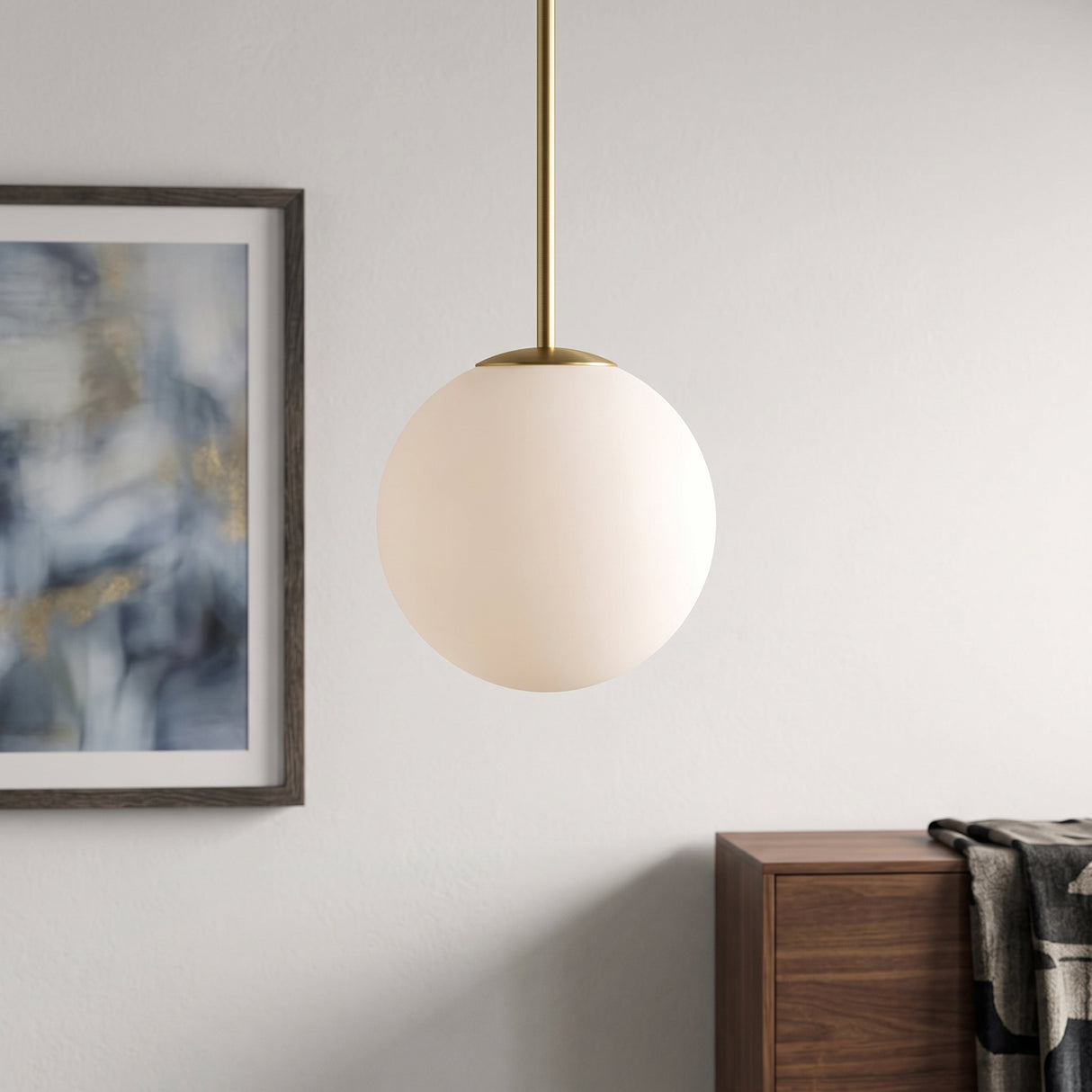 Opal glass globe pendant on slim brass stem beside framed artwork