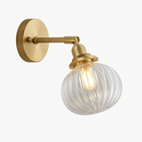 Brass wall sconce with a clear ribbed glass shade and exposed filament bulb
