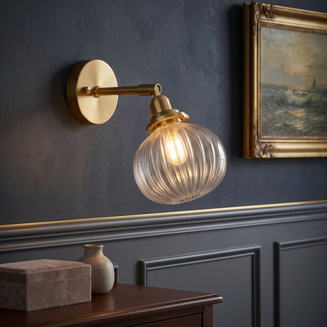 Brass wall sconce with a clear ribbed glass globe on navy panelling
