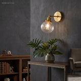 Lit brass sconce with clear ribbed glass beside a dark study bookcase