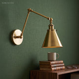 Brass swing arm sconce with a cone shade on a dark green wall