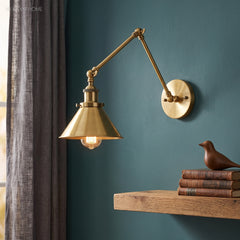 Brass swing arm sconce with a cone shade on a deep teal wall