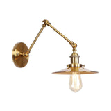 Brass sconce with a flat disc shade and a lit filament bulb