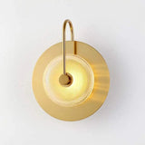 Brass wall sconce with a clear textured glass disc lit on a white wall