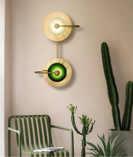 Green glass brass sconces lit on a beige wall above a cactus and chair